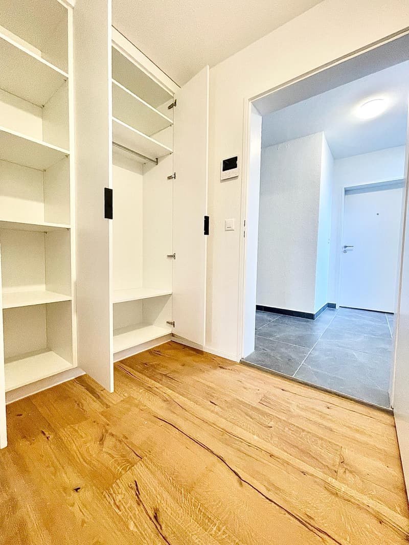 Empty room with wooden floor, white walls, large closet, and an open door leading to another room