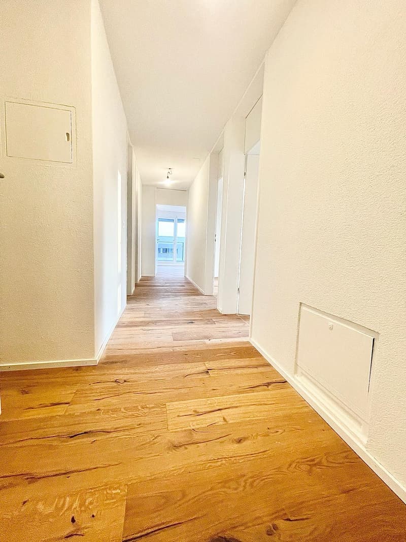Empty hallway with wooden floor, white walls, and doors on both sides