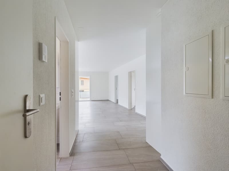 Empty hallway with tiled floor, white walls, and doors on both sides.