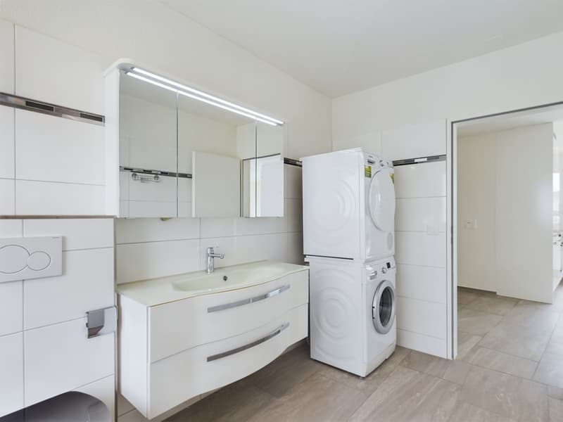 modern bathroom with white tiles, white cabinets, sink, mirror, washing machine, dryer, toilet