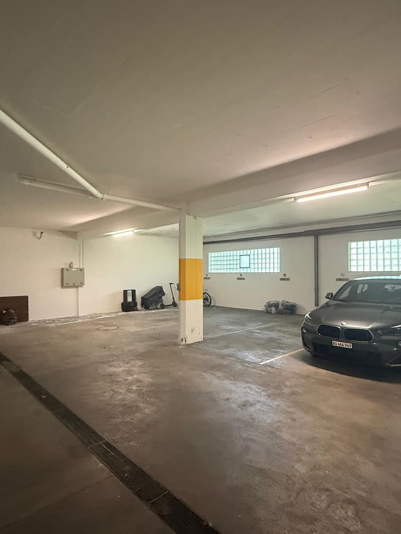 underground parking lot, white walls, concrete floor, white ceiling, a car parked, a scooter, a bicycle, a trash can, a pillar