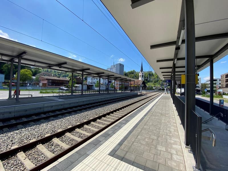 Two tracks, brick paved platform, covered walkway, overhead electrical wires, benches