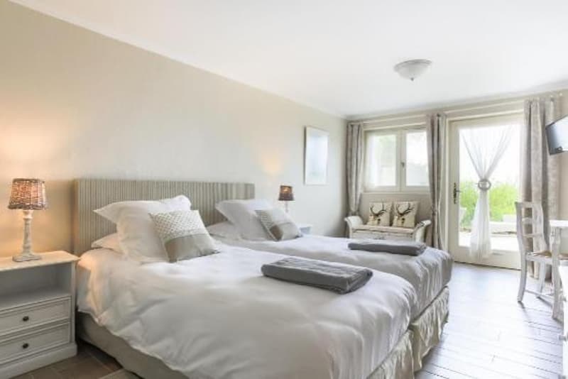 Two twin beds, white bedding, bedside tables with lamps, wooden floor, sliding glass doors to balcony, armchair, TV, desk, and chair