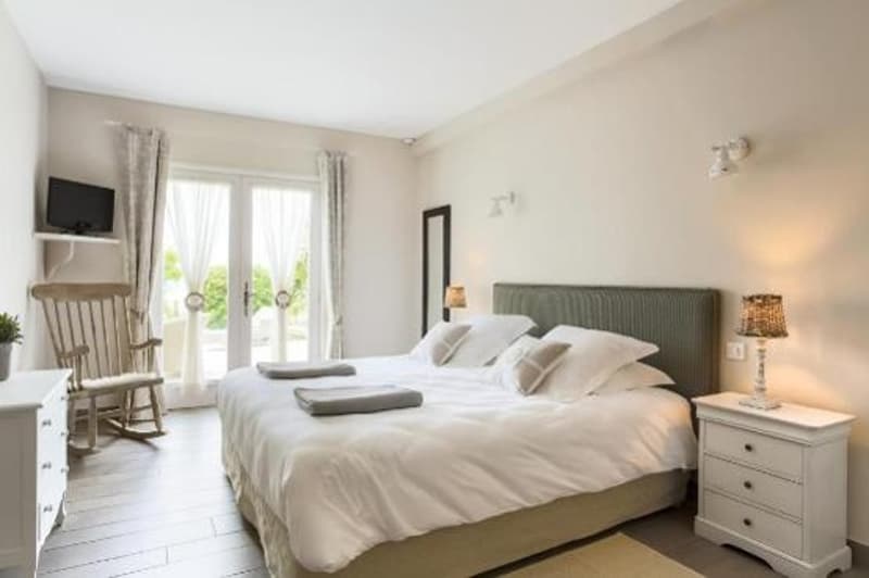 white walls, wooden floor, large bed, bedside tables, lamp, rocking chair, TV, curtains, mirror, balcony