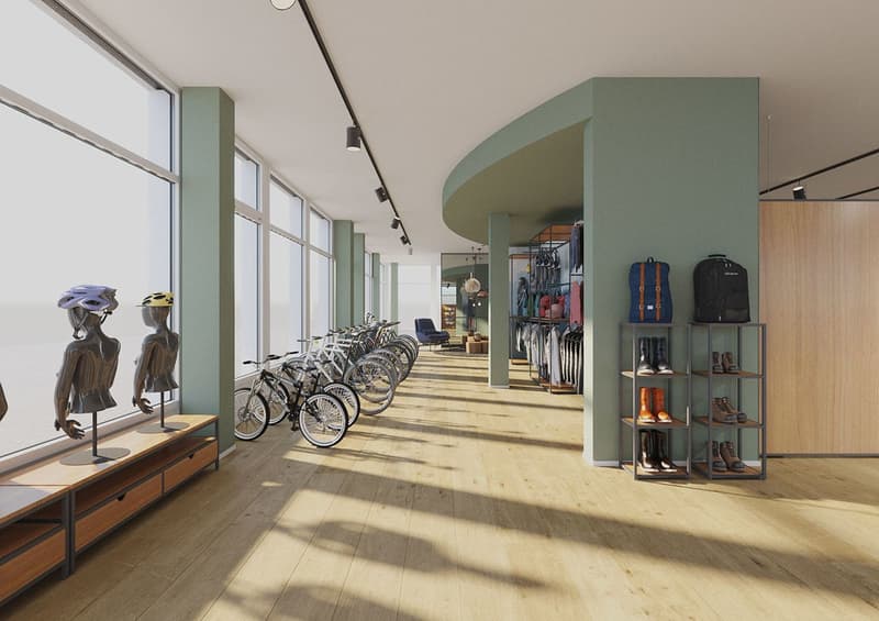 Large open space with hardwood floors, floor-to-ceiling windows, and display racks for clothing and accessories. Several bicycles are parked along the side of the room, indicating a parking area or storage for customers. The space has a modern, minimalist