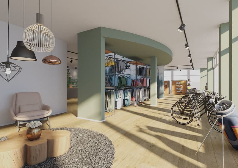 Spacious retail store with modern interior design, featuring a seating area with a comfortable chair, hanging light fixtures, and a display of clothing racks. The store also has a bicycle parking area visible.