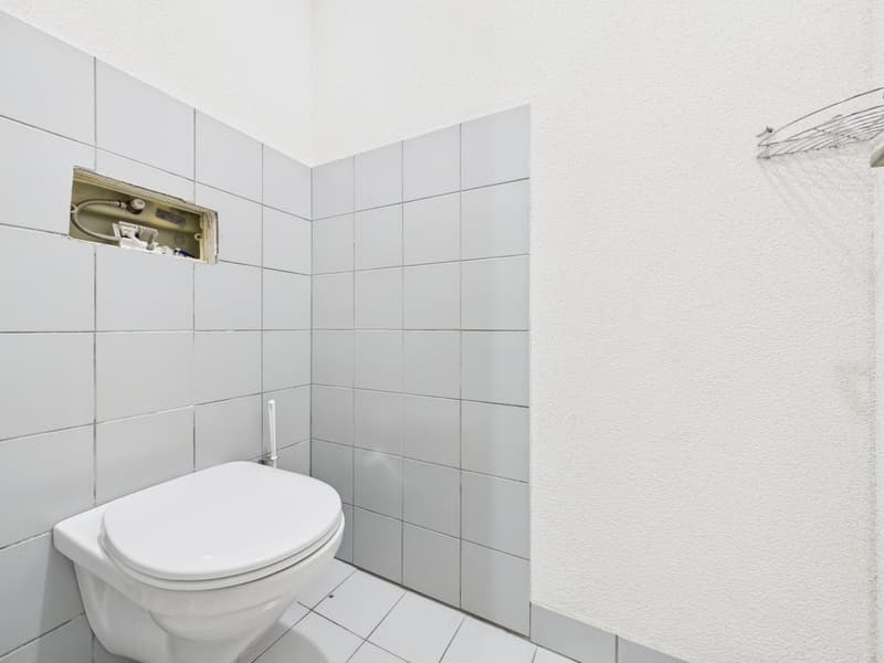 white tiles, white toilet, exposed wiring in the wall, white wall