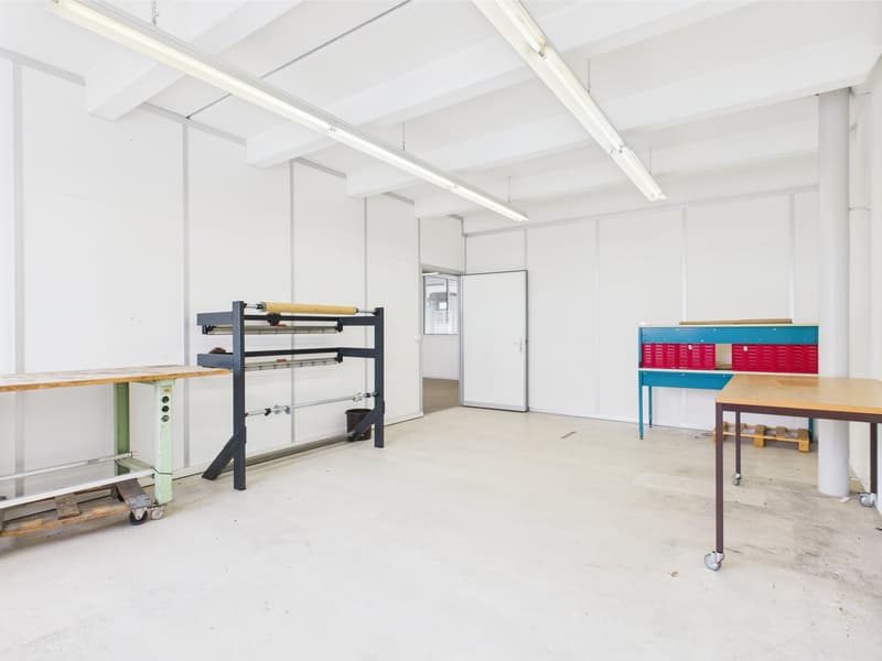 Empty room, industrial styled with white walls and ceiling, large floor area, fluorescent lighting, two wheeled tables, large shelving unit