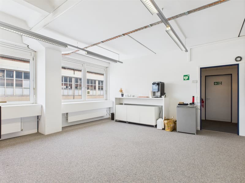 Large, empty room with high ceilings, large windows, wooden desk, radiator, carpeted floor