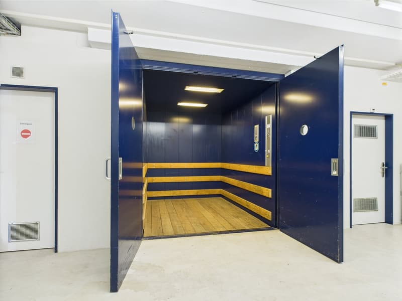 A blue elevator with a wooden interior and an open door