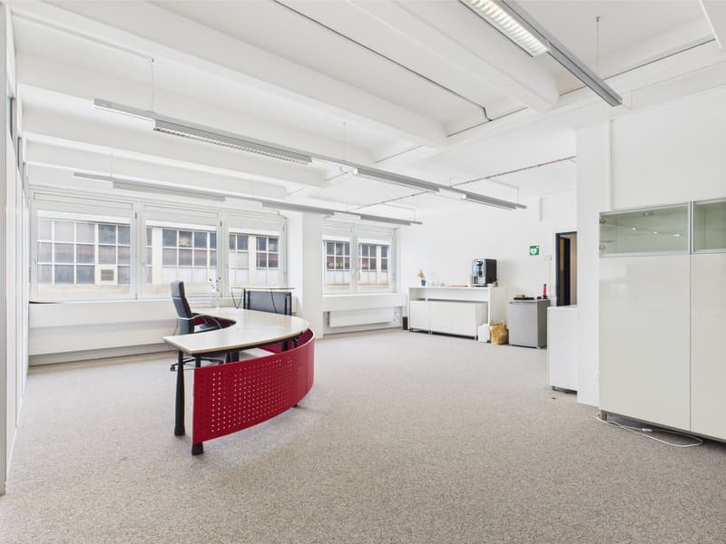 A minimalist office room with large windows, grey carpet, modern furniture, and ample natural light