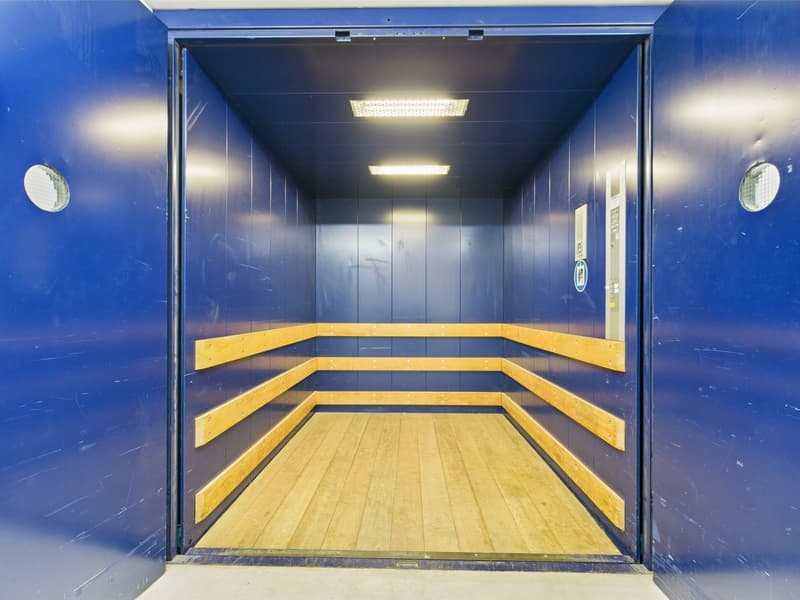 elevator with blue walls, wooden seating, ceiling with lights, grey floor