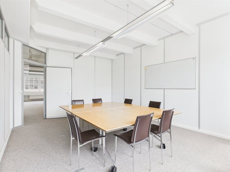 empty conference room with a white wall, white ceiling, carpeted floor, long wooden table, eight brown chairs, whiteboard, sliding door, overhead lights