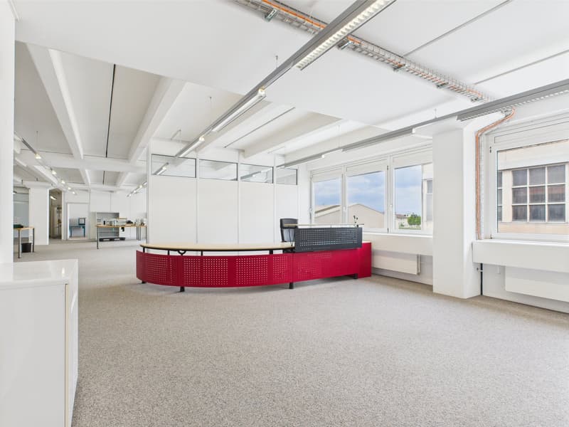 Empty office with high ceilings, red reception desk, white walls, fluorescent lights, large windows
