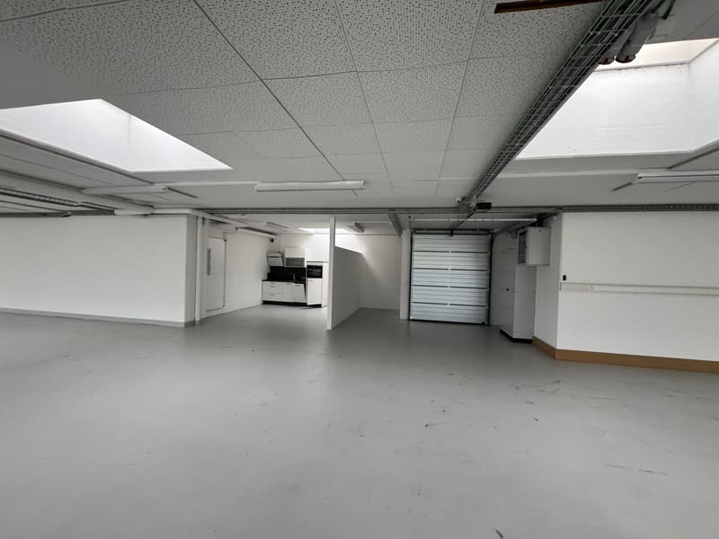 large room with bright lighting, white walls, floor, ceiling with spotlights, garage with automatic door