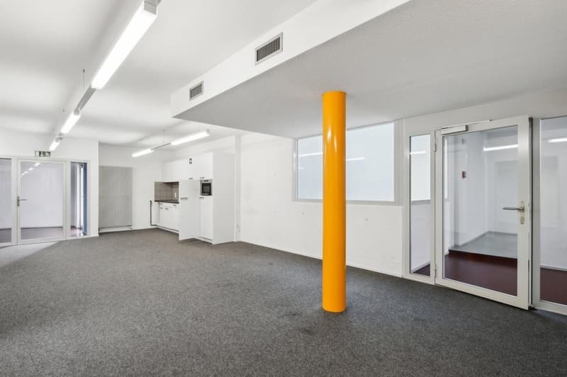 Empty room with sliding doors, radiators, ceiling mounted lights, single central pillar, open kitchen with appliances.