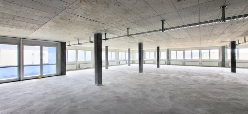 Unfurnished room with concrete walls, pillars, and large windows. Floor is concrete and empty
