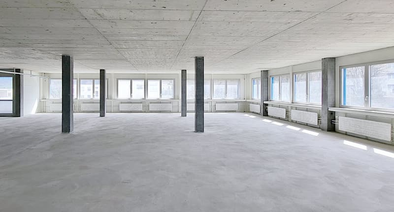 large room, concrete floor, white walls, several windows, central heating radiators, pillars