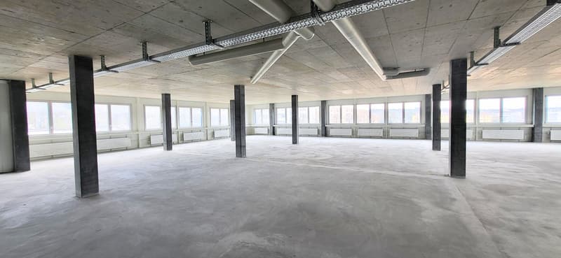 large open space with multiple windows, radiators along the walls, concrete flooring, beams and ductwork on the ceiling