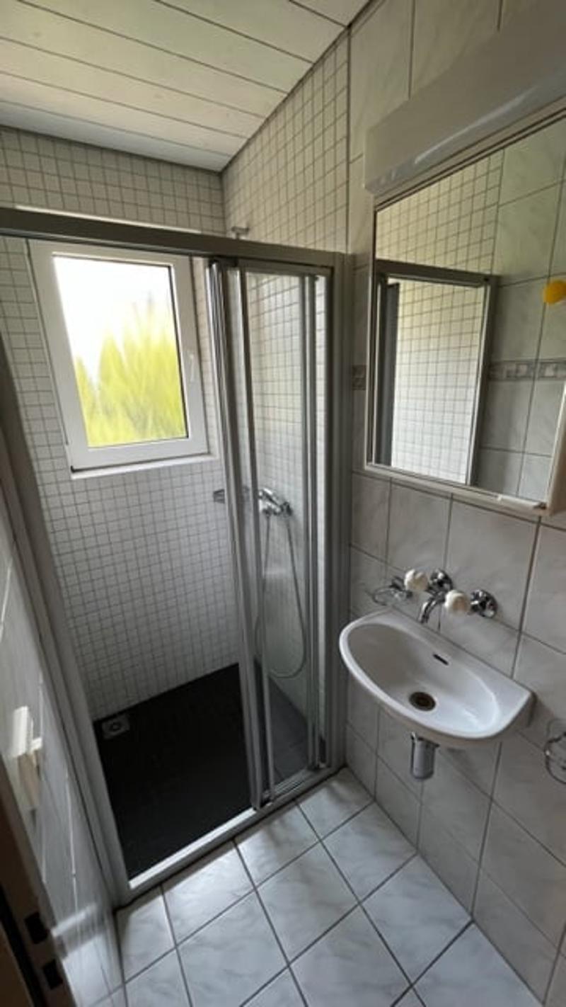 Tiled bathroom with a shower enclosure, sink, and window providing natural light.