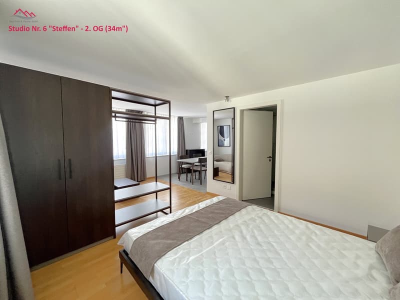 Bedroom with bed, large wardrobe, mirror, and small table with chairs in a room.