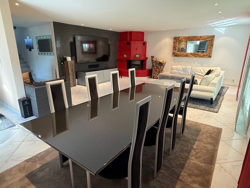 Modern and stylish living room with a large dining table, black chairs, a red fireplace, and a couch. The room has a sleek and contemporary design with a large TV mounted on the wall and decorative elements like the framed artwork.