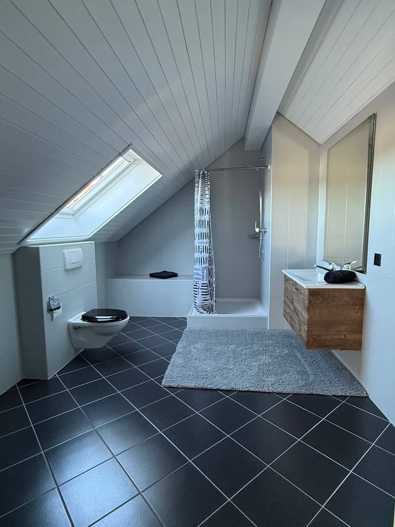 Bathroom with slanted ceiling, grey tile flooring, walk-in shower, vanity with wooden cabinet, and toilet