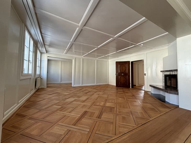 hardwood parquet flooring, fireplace, high ceiling, white walls, wooden door, windows