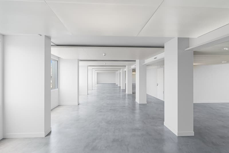 Empty hallway with white walls, gray floor, and white pillars