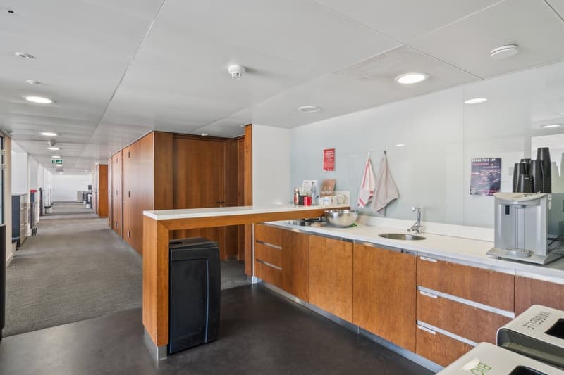 modern kitchen with wooden cabinets, white countertops, stainless steel sink, faucet, trash bin, coffee machine, and a bowl on the counter