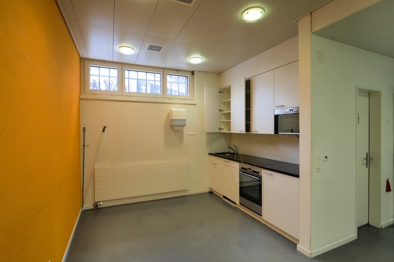Empty kitchen with white cabinetry, grey floor, yellow wall, two windows, and a dishwasher and washing machine.