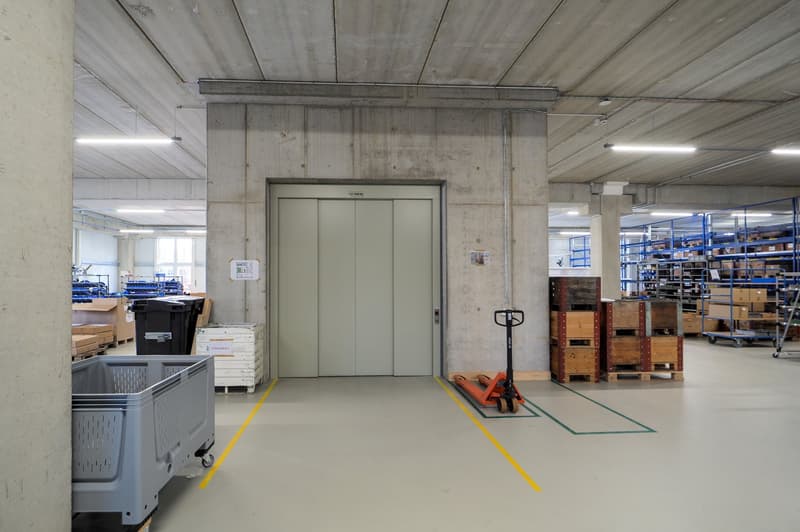 Wide open space, elevated floors, double door elevator, yellow and green lines marking floor, storage boxes and trolleys