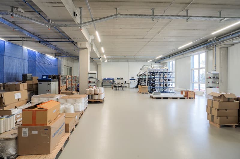 large warehouse, bright lighting, various equipment and storage boxes, white floor, blue covering on the left side