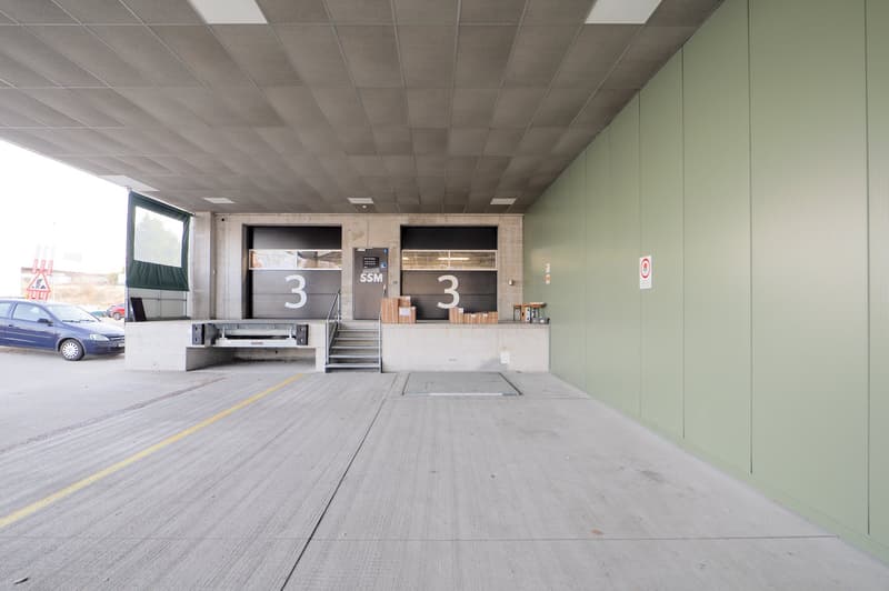 Parking lot with two stalls and stairs, car in stall, number 3 on stalls, green walls, cement floor