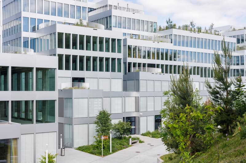 Multi-story modern office building with glass facades, balconies, and landscaped outdoor areas