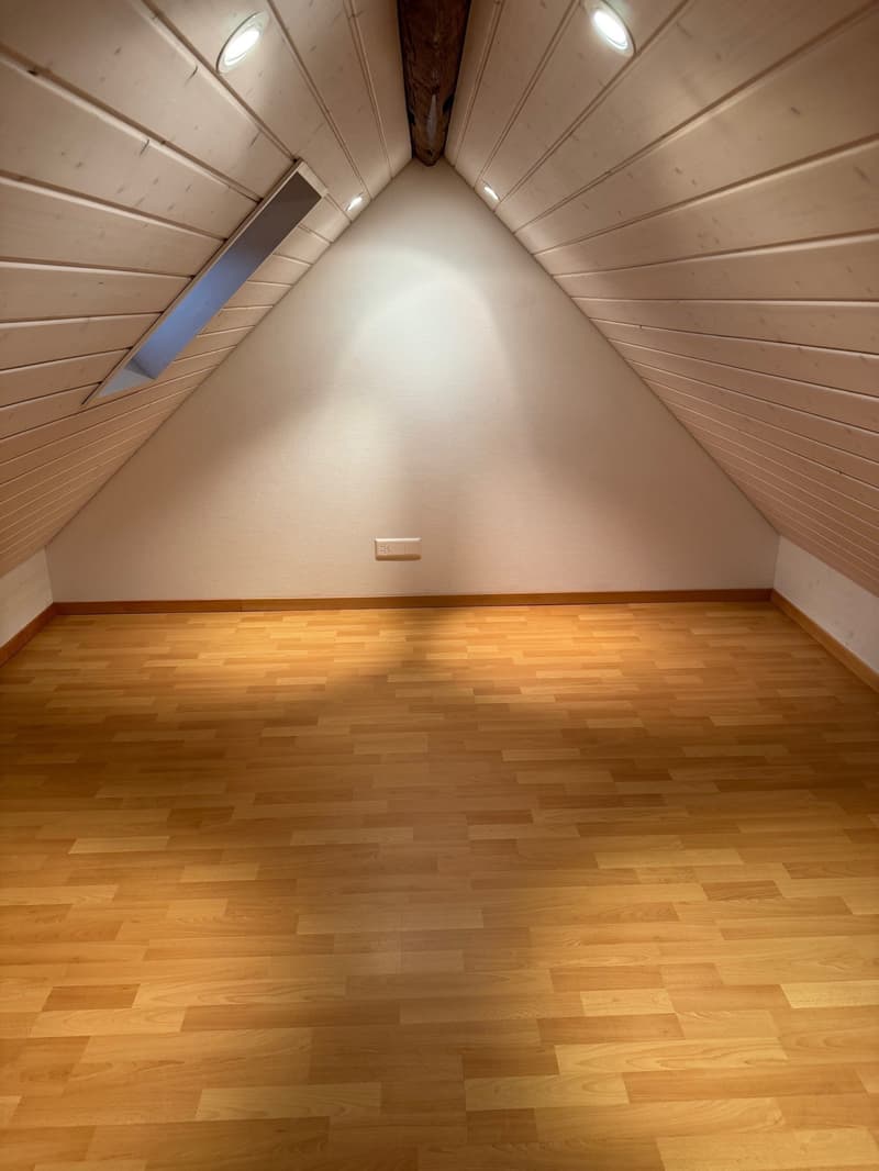 empty attic room with wooden floor, white walls, wooden ceiling, and a window