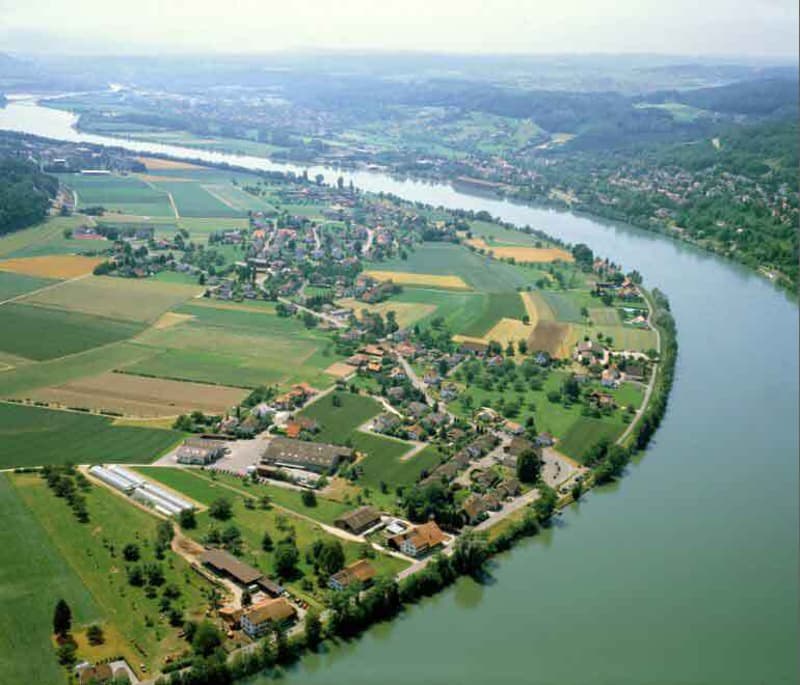 Aerial view of a village with houses, green fields, and a river