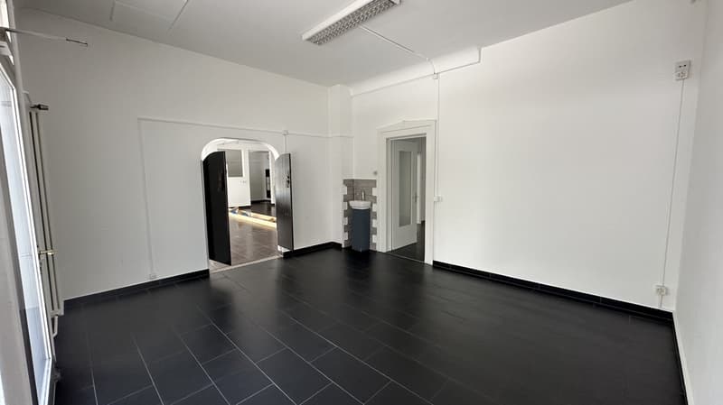 Empty room with black floor and white walls, sink and door