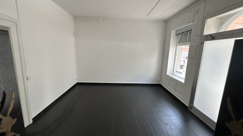 Empty room with white walls, black floor, two windows, and two doors.