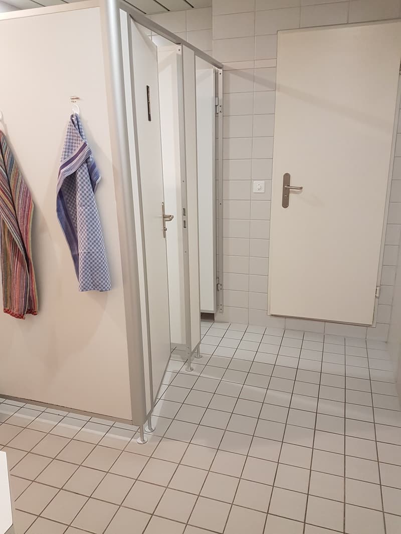 public washroom with white tiled floor, white doors, white walls and towels on hooks