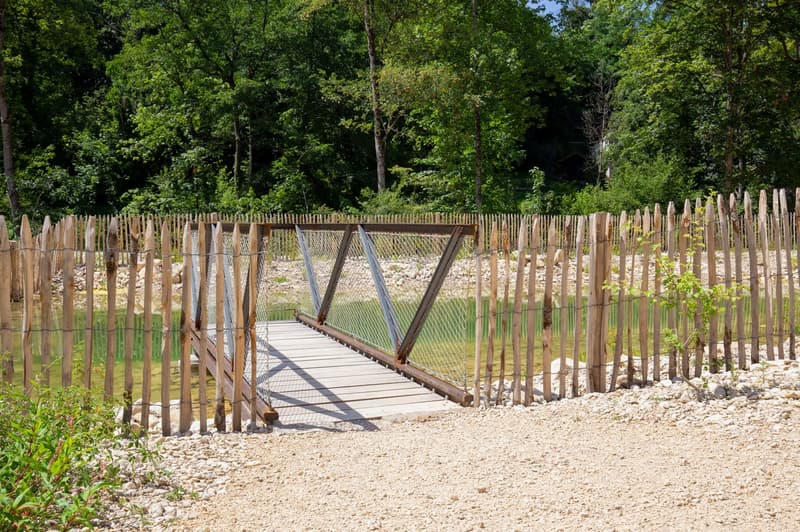 Wooden fence, wooden bridge with a metal frame, gravel pathway, greenery