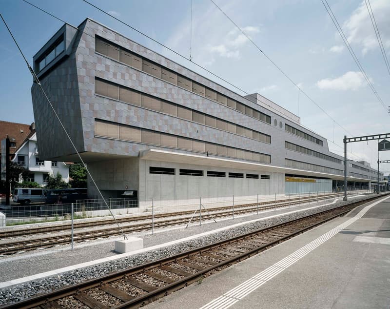 large gray and brown building, multiple windows, next to railroad track