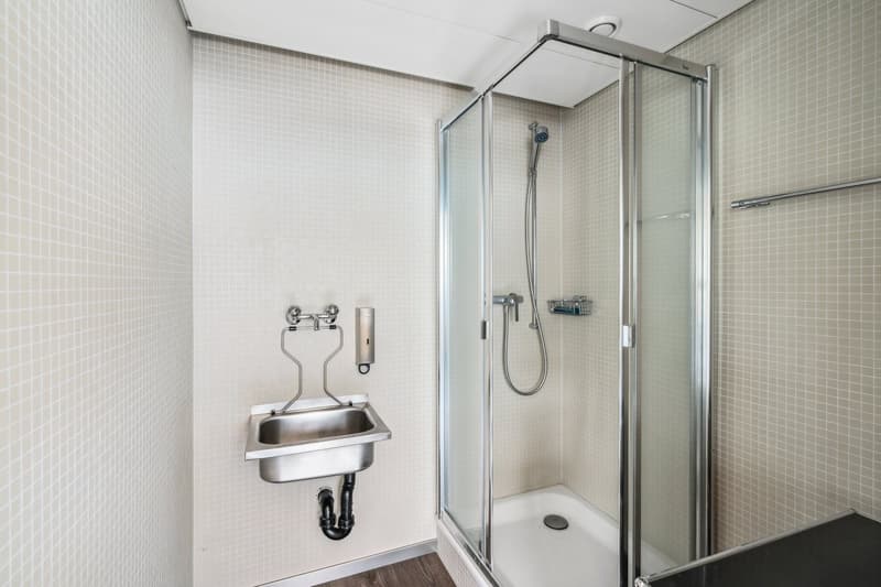 A small bathroom with a glass walk-in shower, a stainless steel sink, and a tiled wall.