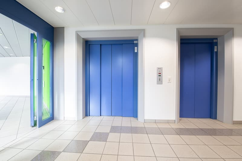 Two blue elevators with doors, two buttons, tiled floor