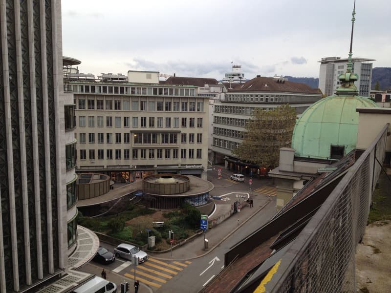 Aerial view of a city with multiple buildings, a green dome, and a road with cars and people walking.