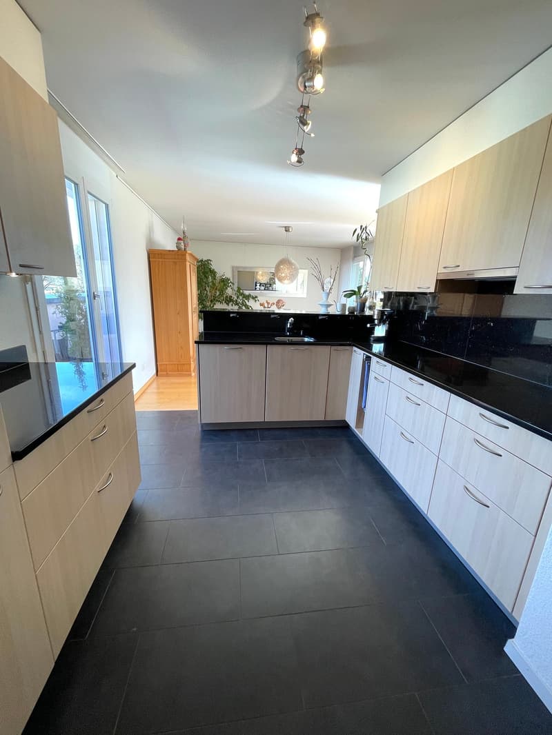 Spacious kitchen with light wood cabinets, black countertops, and a dishwasher. The kitchen has a modern and open layout with a track lighting fixture overhead.