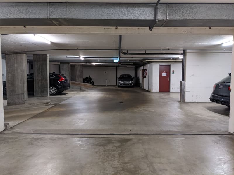 underground parking lot with concrete floor, 3 cars parked, fire extinguisher, metal railings, white walls