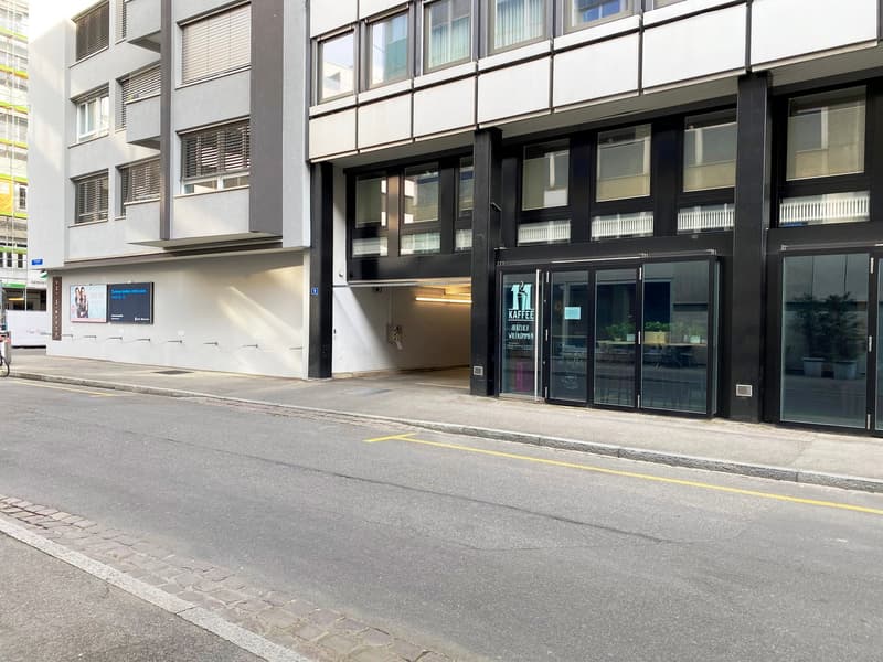 Modern building with glass doors, entrance to a garage, glass windows, and a sidewalk