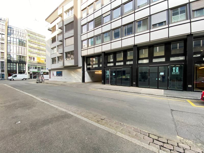 Modern multi-story building with glass windows, entrance with glass doors, and a sign reading 'KAFFEE'.