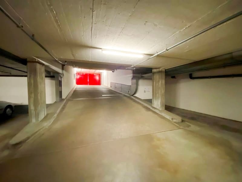Empty parking lot with concrete floor, white walls, and a red exit door.